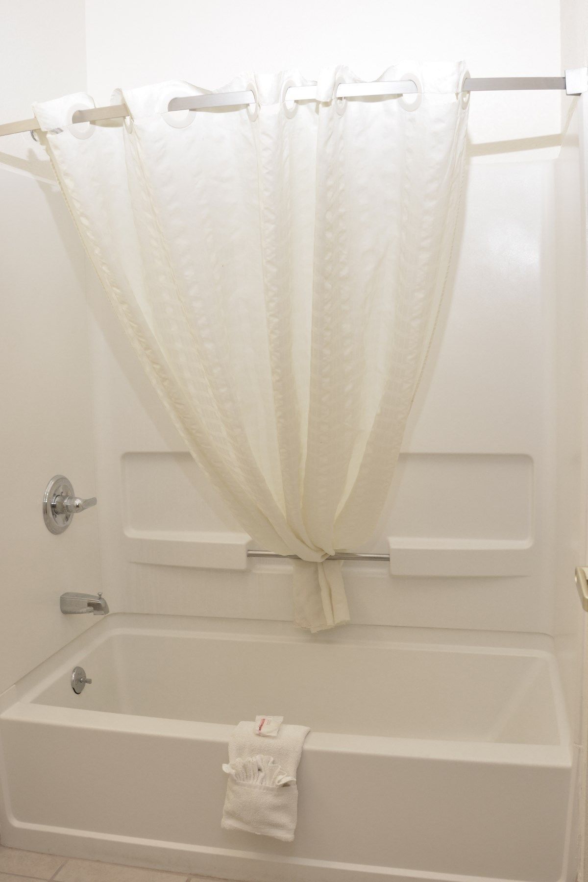 A white bathtub with a towel on the side, a shower curtain, and a door with a handle.