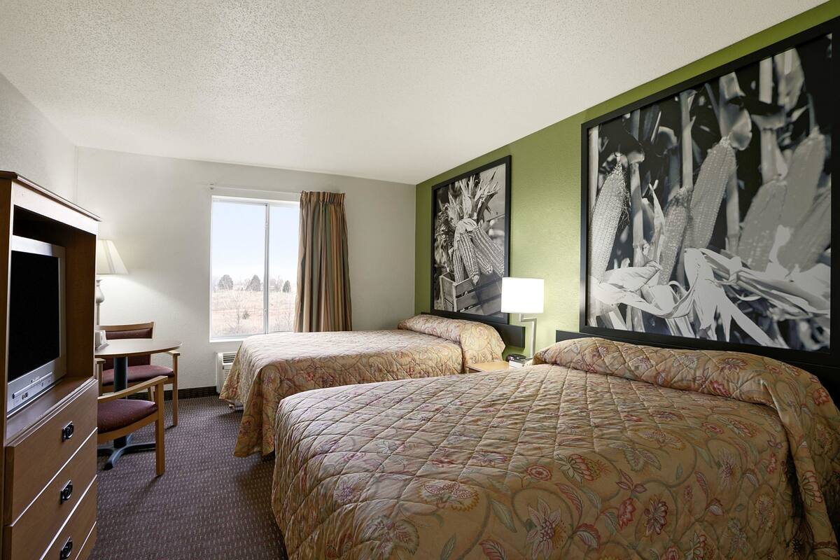 A hotel room with two beds, a TV, a desk, and a large window.