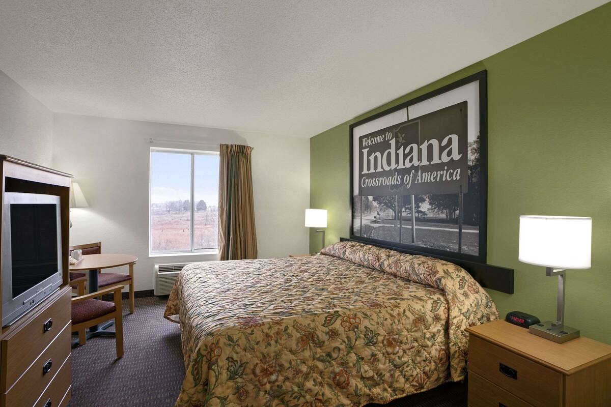 A hotel room with a bed, a desk, a chair, a TV, and a window.