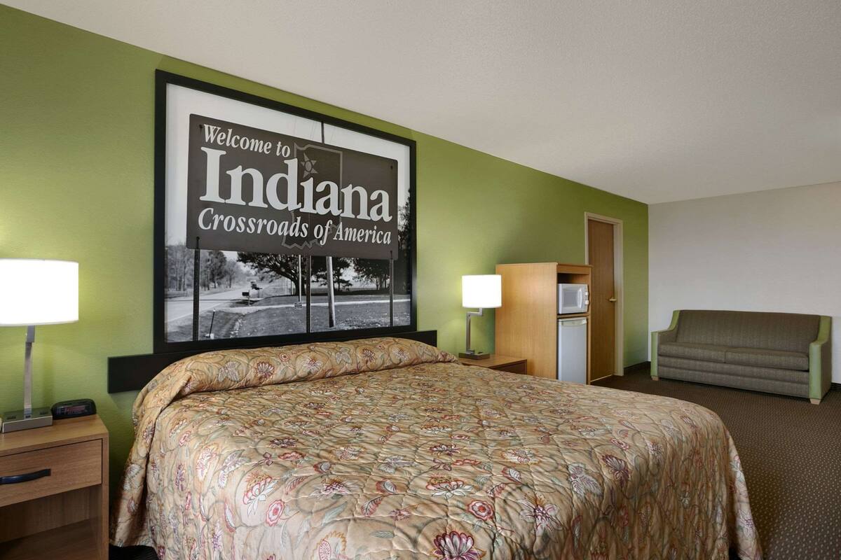 A hotel room with a bed, a nightstand, a lamp, a sofa, and a wall sign.