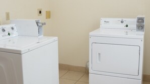 Uma lavanderia com duas máquinas de lavar e secar Whirlpool brancas, piso de azulejo e luminária no teto.