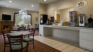 Espaço de café da manhã em hotel, com lareira, mesa de jantar, cadeiras e um canto para café.