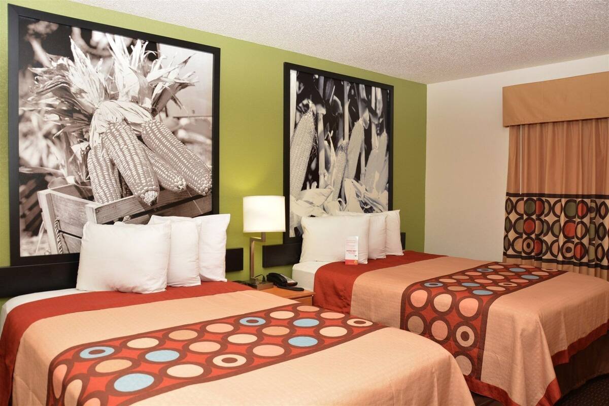 A hotel room with two beds, a nightstand, a lamp, and two large black-and-white photographs on the walls.