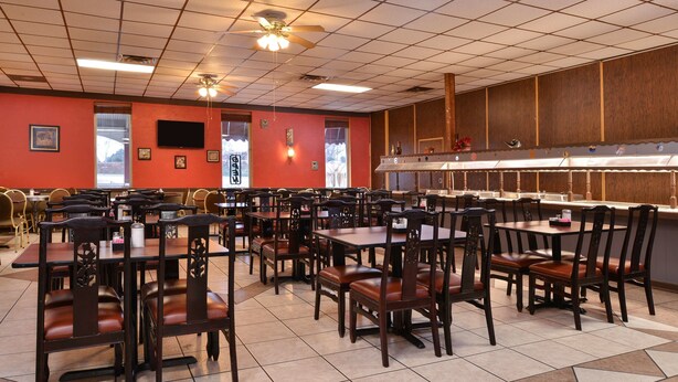 A restaurant with multiple tables and chairs, a kitchen area, and a television on the wall. - Castle Inn & Suites Anadarko (Anadarko)