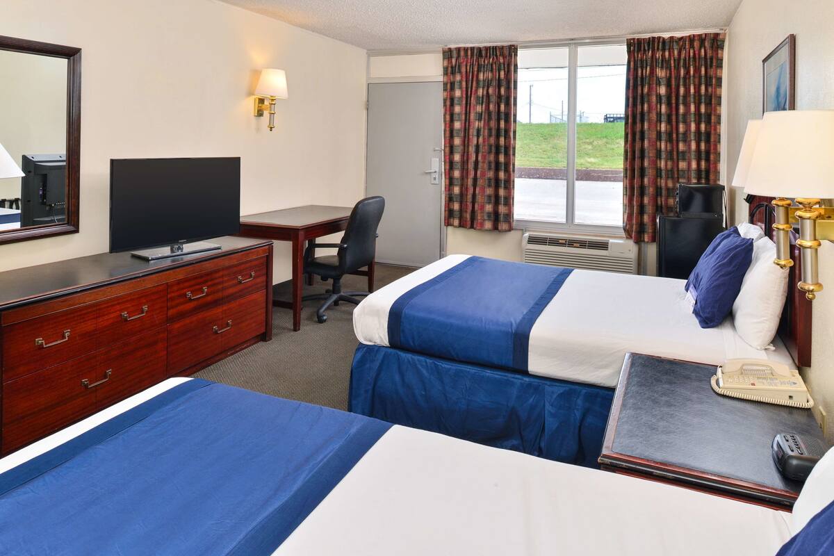 A hotel room with two beds, a desk, a television, a telephone, and a window with curtains.