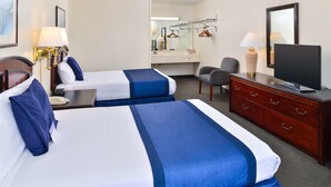 A hotel room with two beds, a desk, a chair, a dresser, a television, and a mirror. - Castle Inn & Suites Anadarko (Anadarko)