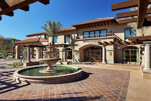 A hotel with a fountain in the courtyard, a covered walkway, and a clear blue sky.