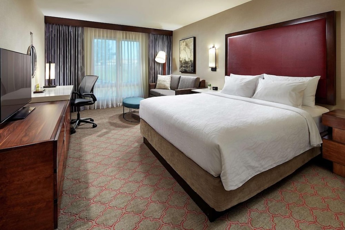 Een hotelkamer met een groot bed, een bureau met een flatscreen televisie, een stoel en een bijzettafeltje.
