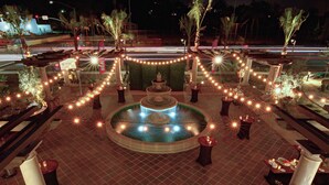 Une fontaine entourée de tables et de chaises, agrémentée de guirlandes lumineuses et de palmiers.