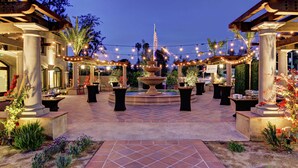 Un espace extérieur aménagé en patio, avec une fontaine centrale, des guirlandes lumineuses et des plantes en pot.