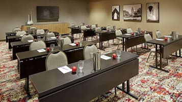 A conference room with multiple tables and chairs, a large flat-screen TV on the wall, and framed pictures.