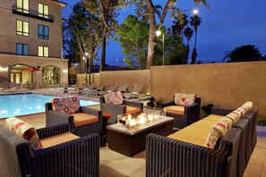 A poolside area with wicker furniture, a fire pit, and a view of the pool and building in the background.
