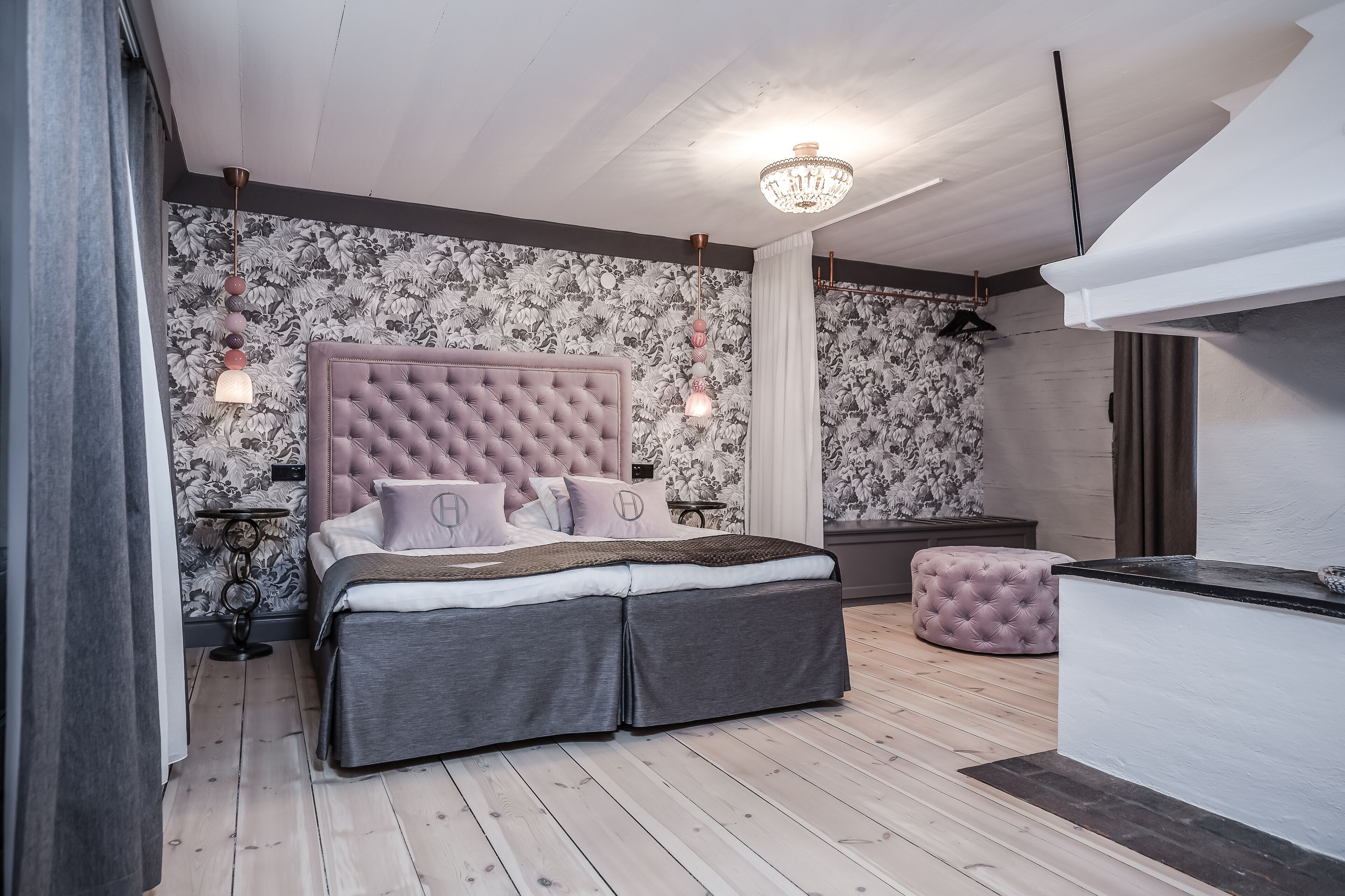 A bedroom with a tufted headboard, a bed with grey bedding, a pink ottoman, and a chandelier.