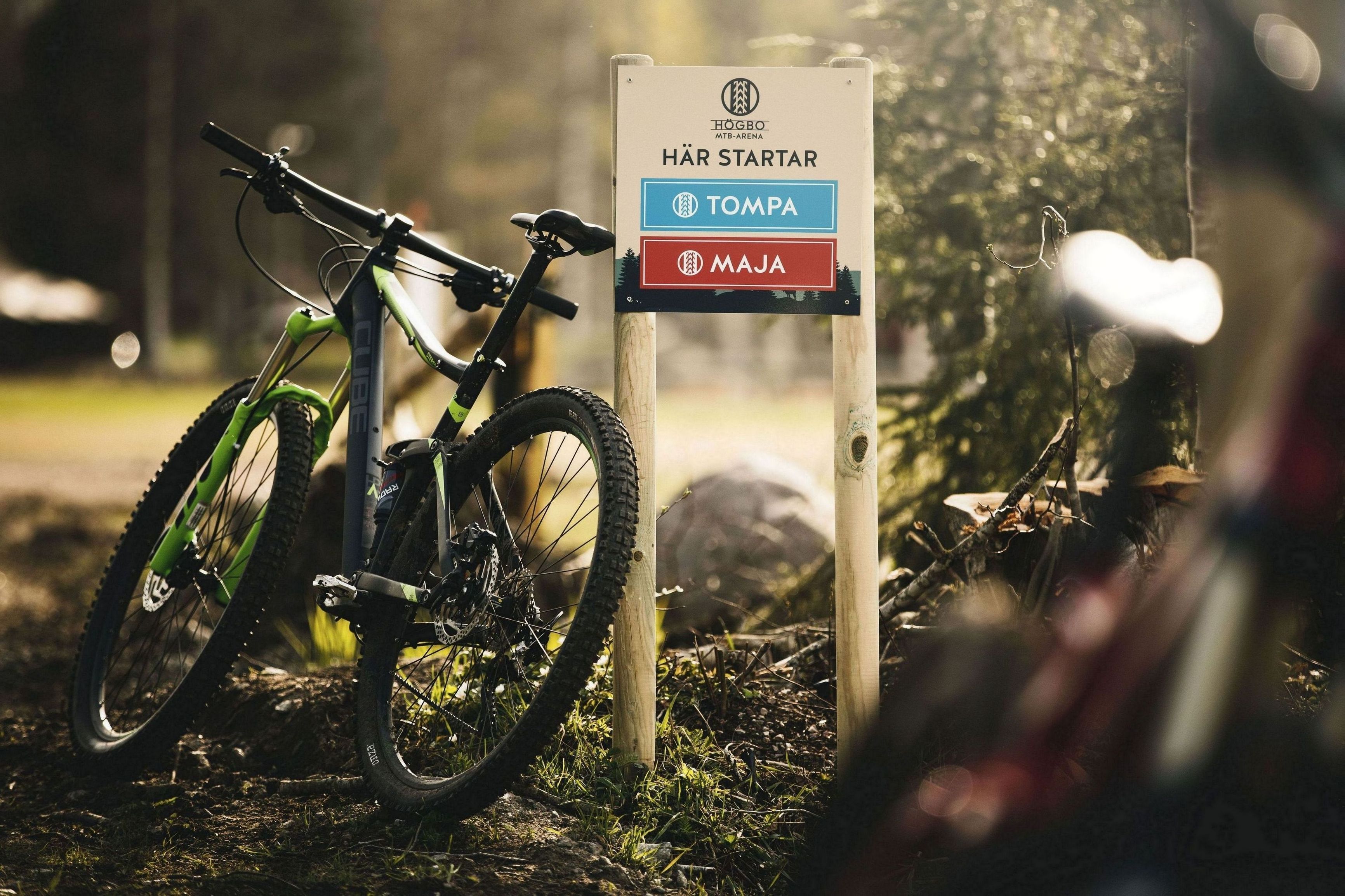 Una bicicleta de montaña estacionada junto a un letrero con indicaciones a 'HÄR STARTAR' (EMPIEZA AQUÍ), 'TOMPA' y 'MAJA'.