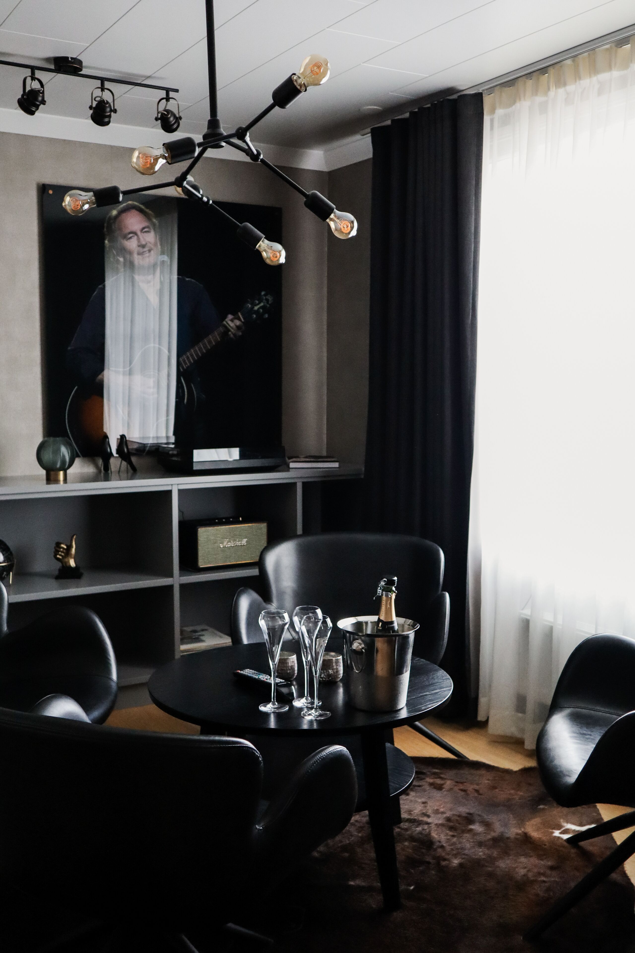 Un salon moderne avec un canapé en cuir noir, une table à manger ronde agrémentée de verres à vin et d’une bouteille, et un téléviseur fixé au mur.