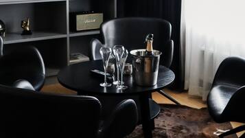 Un salon moderne avec un canapé en cuir noir, une table à manger ronde agrémentée de verres à vin et d’une bouteille, et un téléviseur fixé au mur.