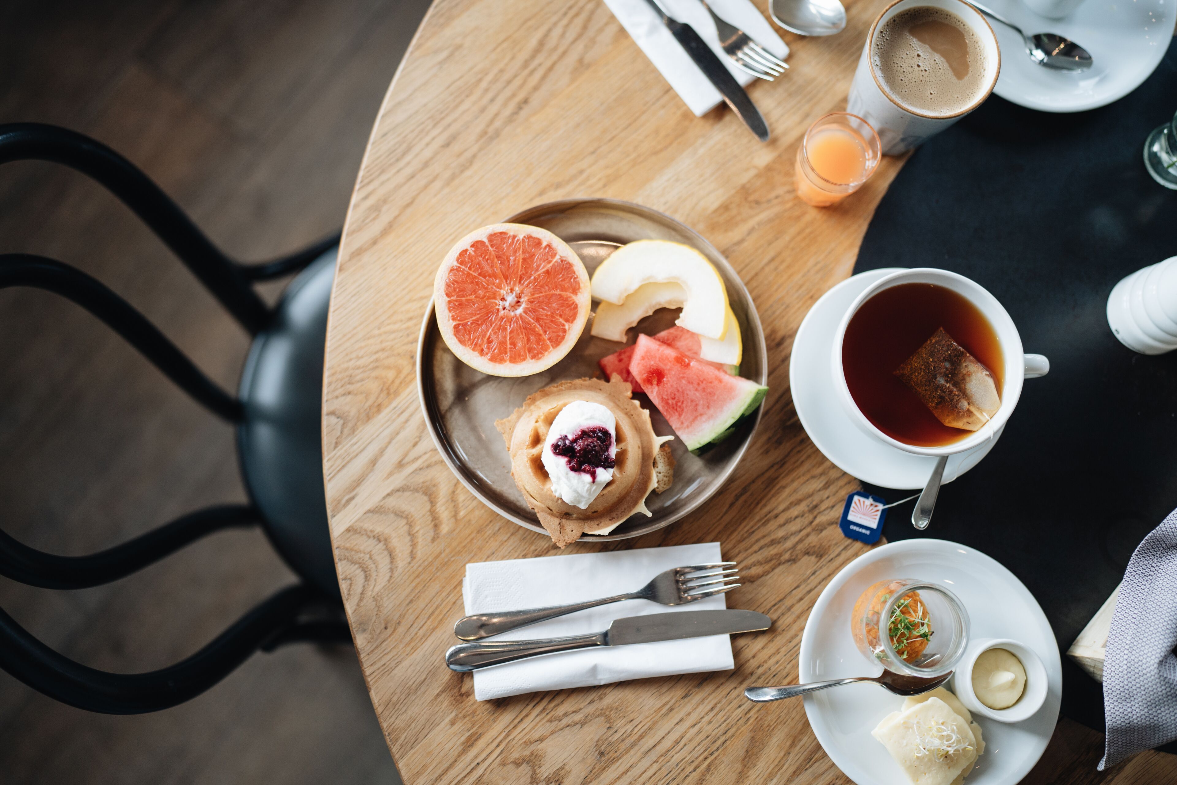 A breakfast setting with a plate of food, a cup of tea, and a glass of orange juice on a wooden table.