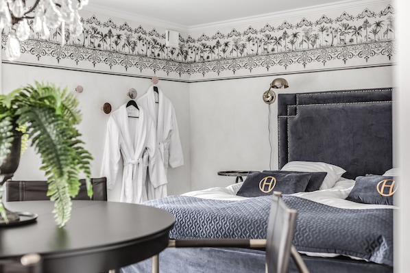 A hotel room with a bed, a table, and a chair. There is a plant on the table and a coat rack with clothes hanging on it. - Högbo Brukshotell & Spa (Sandviken)