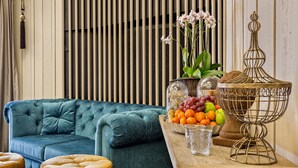 Un sofá color turquesa, una mesa de madera con un cuenco de frutas, un vaso y un recipiente metálico decorativo.