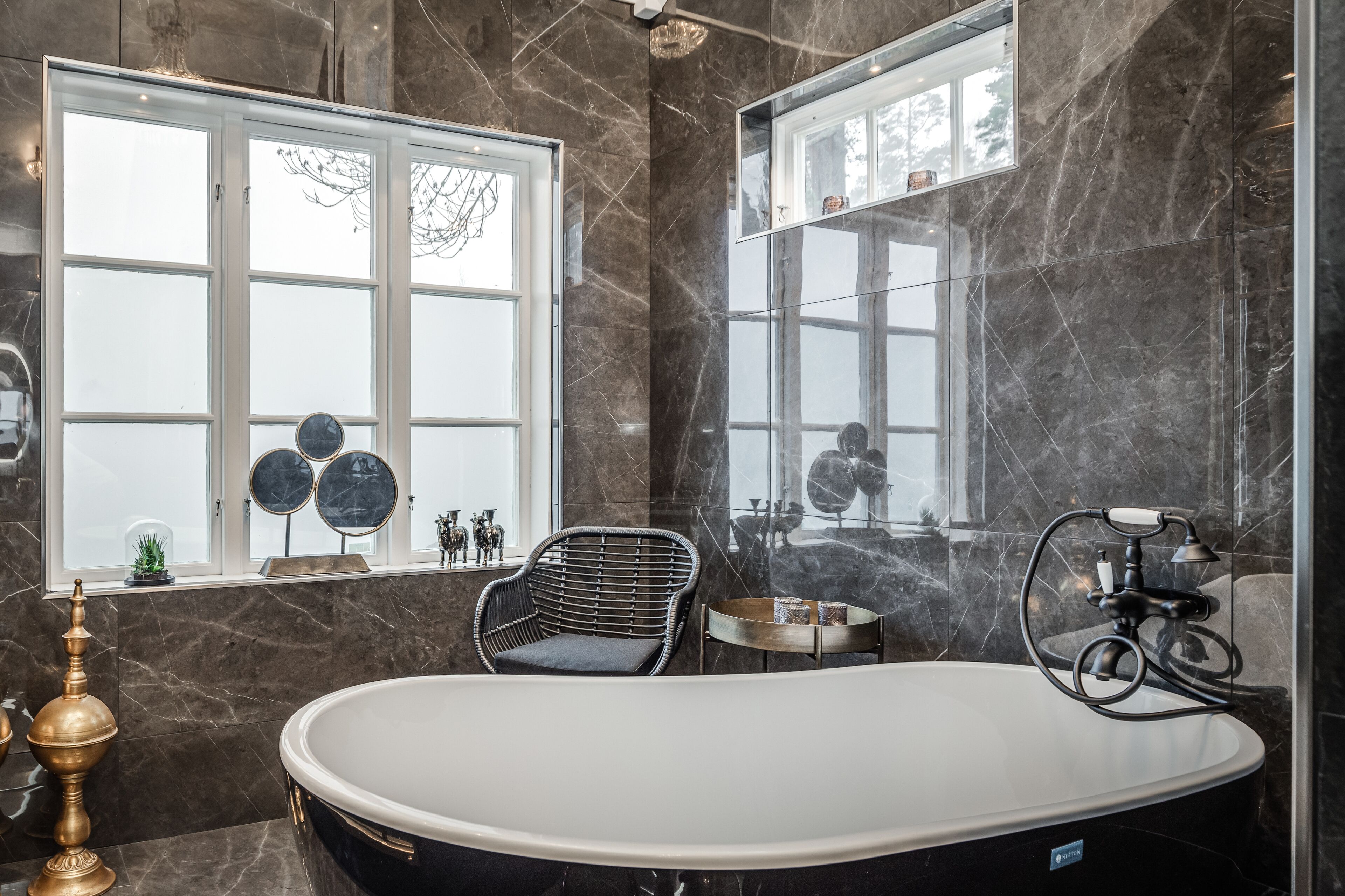 Ein modernes Badezimmer mit einer freistehenden Badewanne, einem Fenster mit dekorativen Spiegeln und einer Marmorwand.