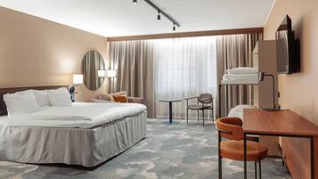 A hotel room with a bed, a desk, a chair, a TV, and a window with curtains.