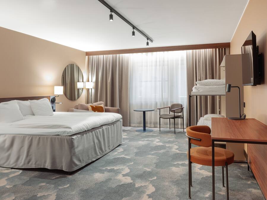 A hotel room with a bed, a desk, a chair, a TV, and a window with curtains.