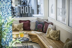 A corner seating area with a wooden bench, cushioned pillows, and a tray with a glass and a candle.