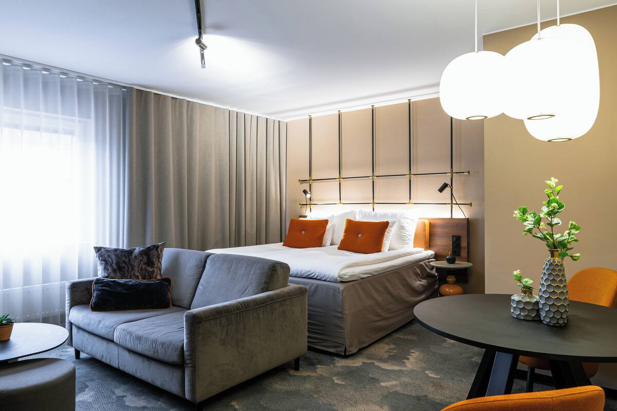 Moderni hotellihuone, jossa on sänky, sohva ja ruokapöytä.
