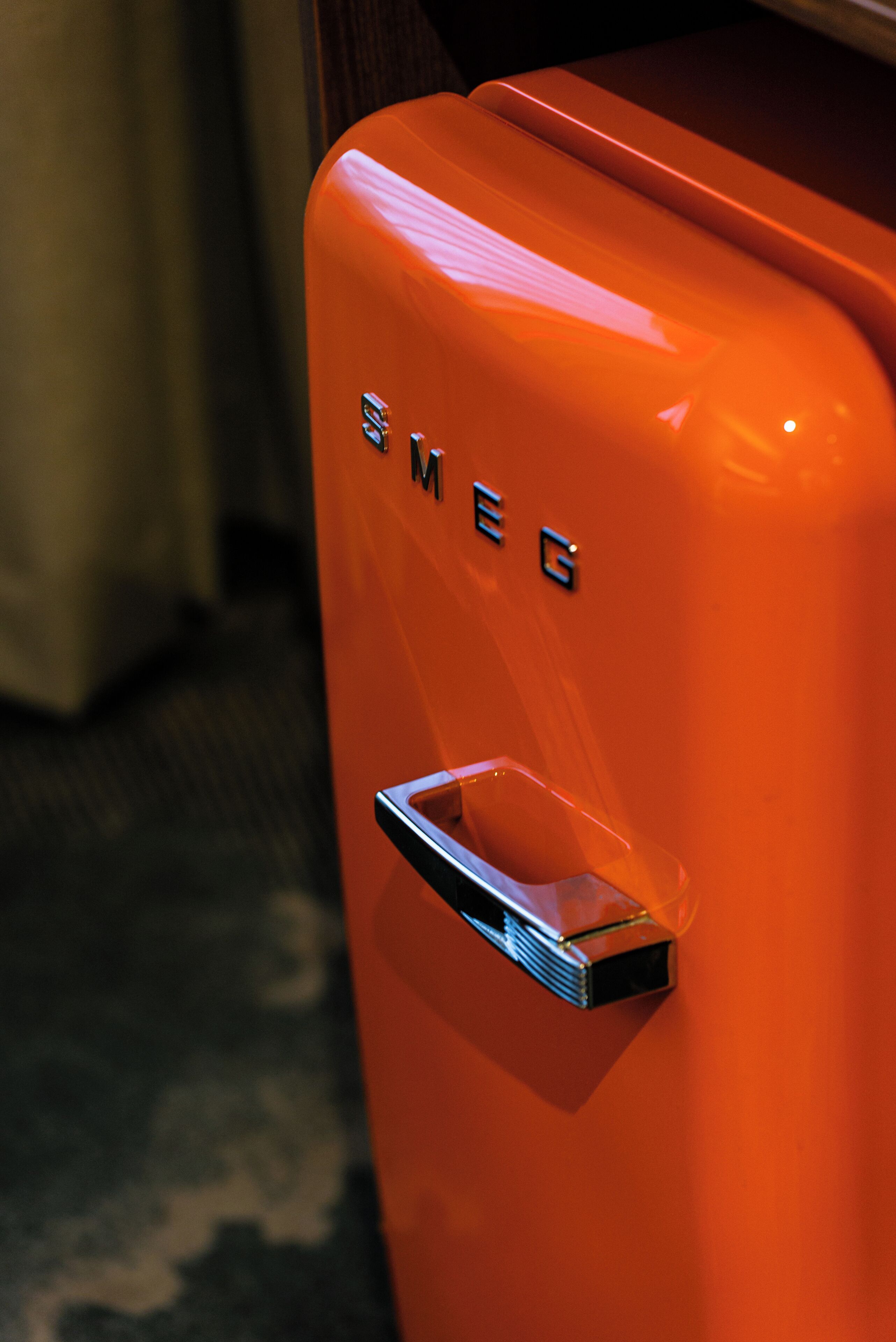 A close-up of a bright orange vintage-style luggage with the label "SMEG" on it.