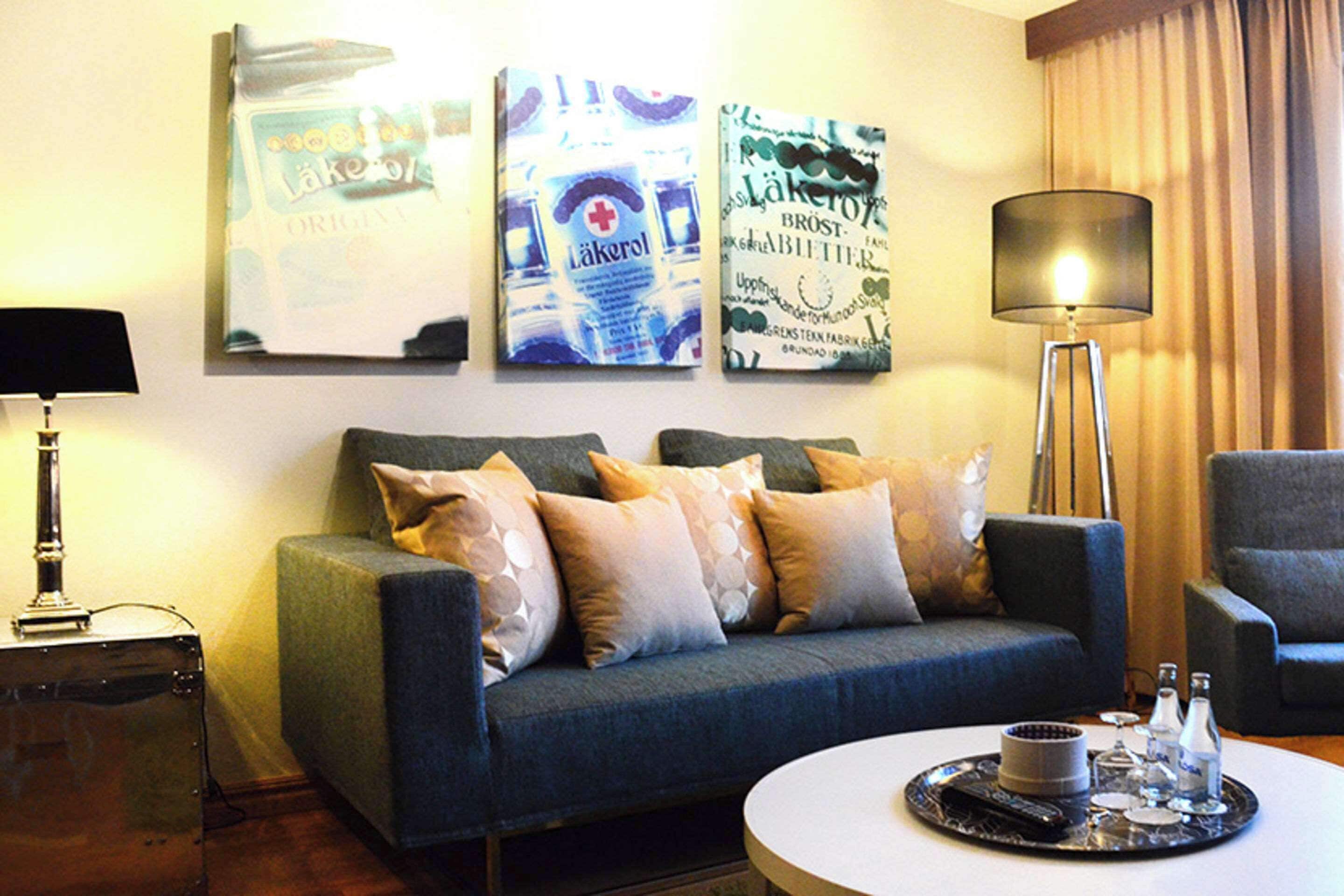 A living room with a sofa, a side table, a lamp, and a tray with bottles and glasses.