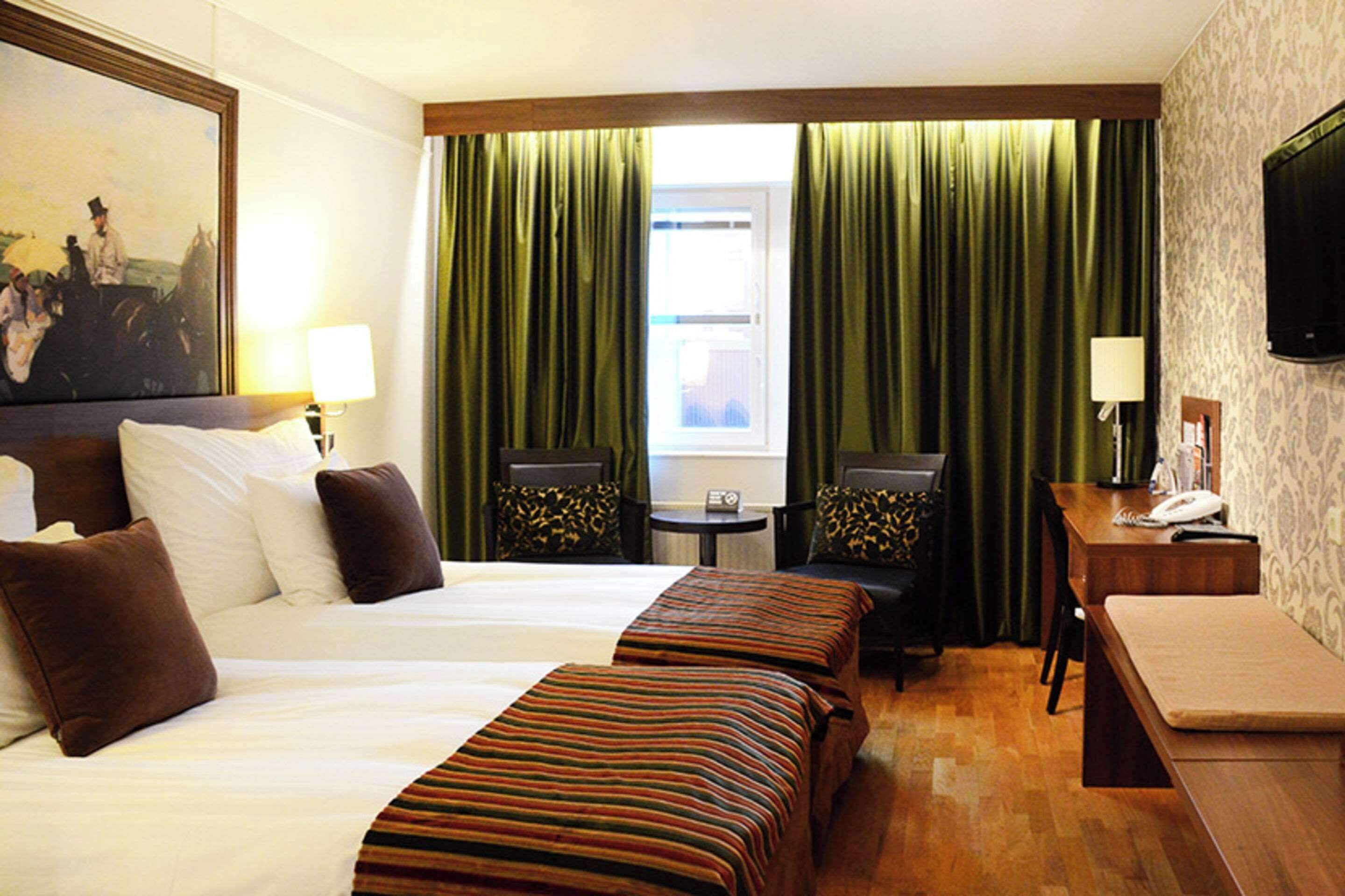 A hotel room with two beds, a desk, a chair, a television, and a window with curtains.