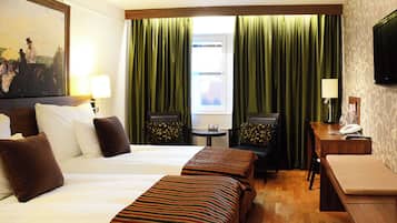 A hotel room with two beds, a desk, a chair, a television, and a window with curtains.