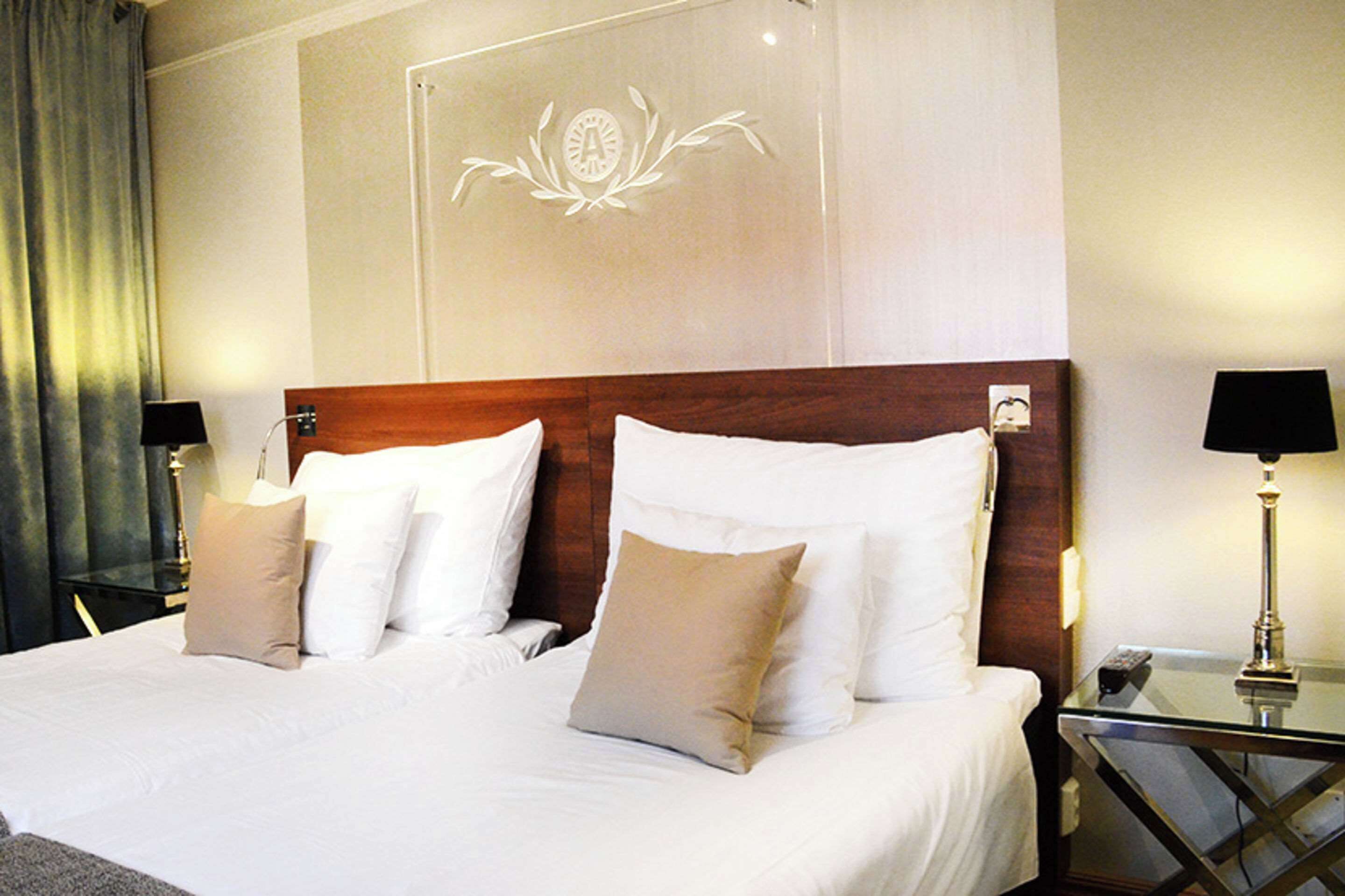 A hotel room with a large bed, two bedside tables, a nightstand, a lamp, and a wall-mounted decoration.