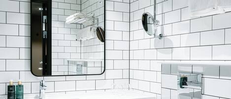 A modern bathroom with white tiled walls, a large mirror, a white sink, and a toilet.