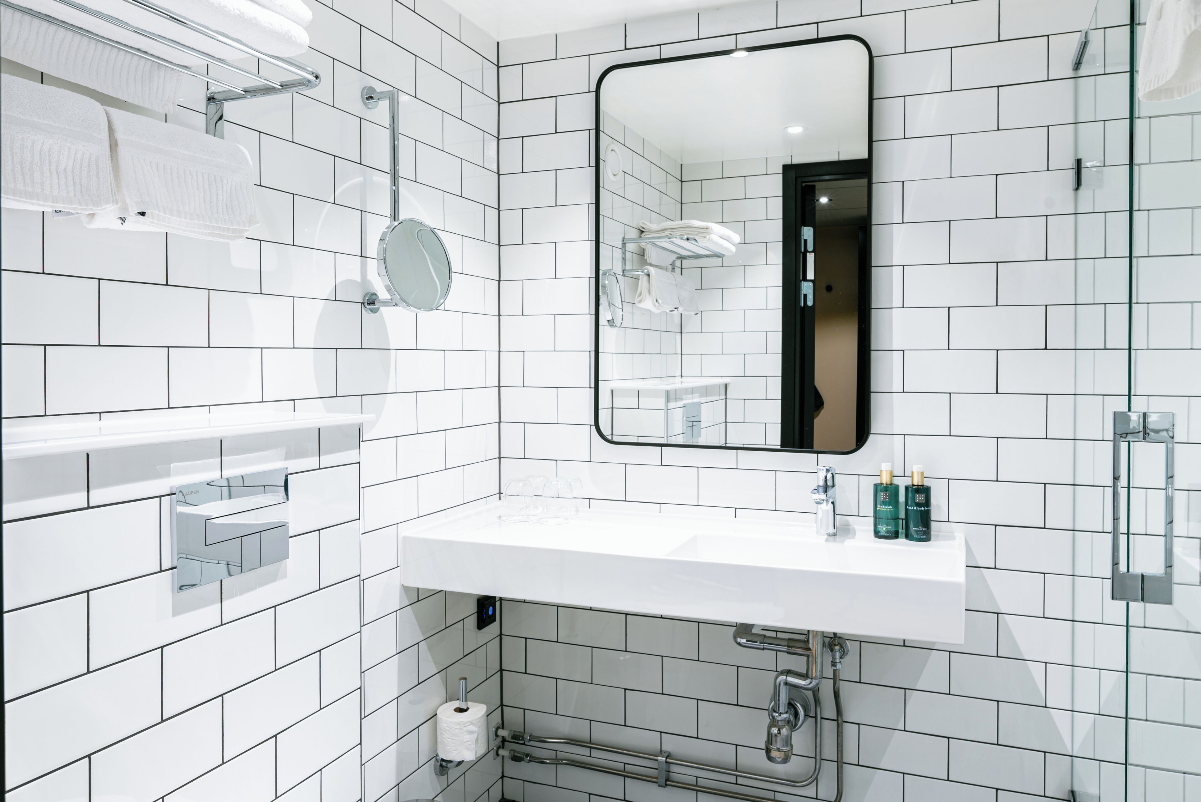 Un baño moderno con paredes de azulejos blancos, un lavabo blanco, un espejo y barras para toallas.