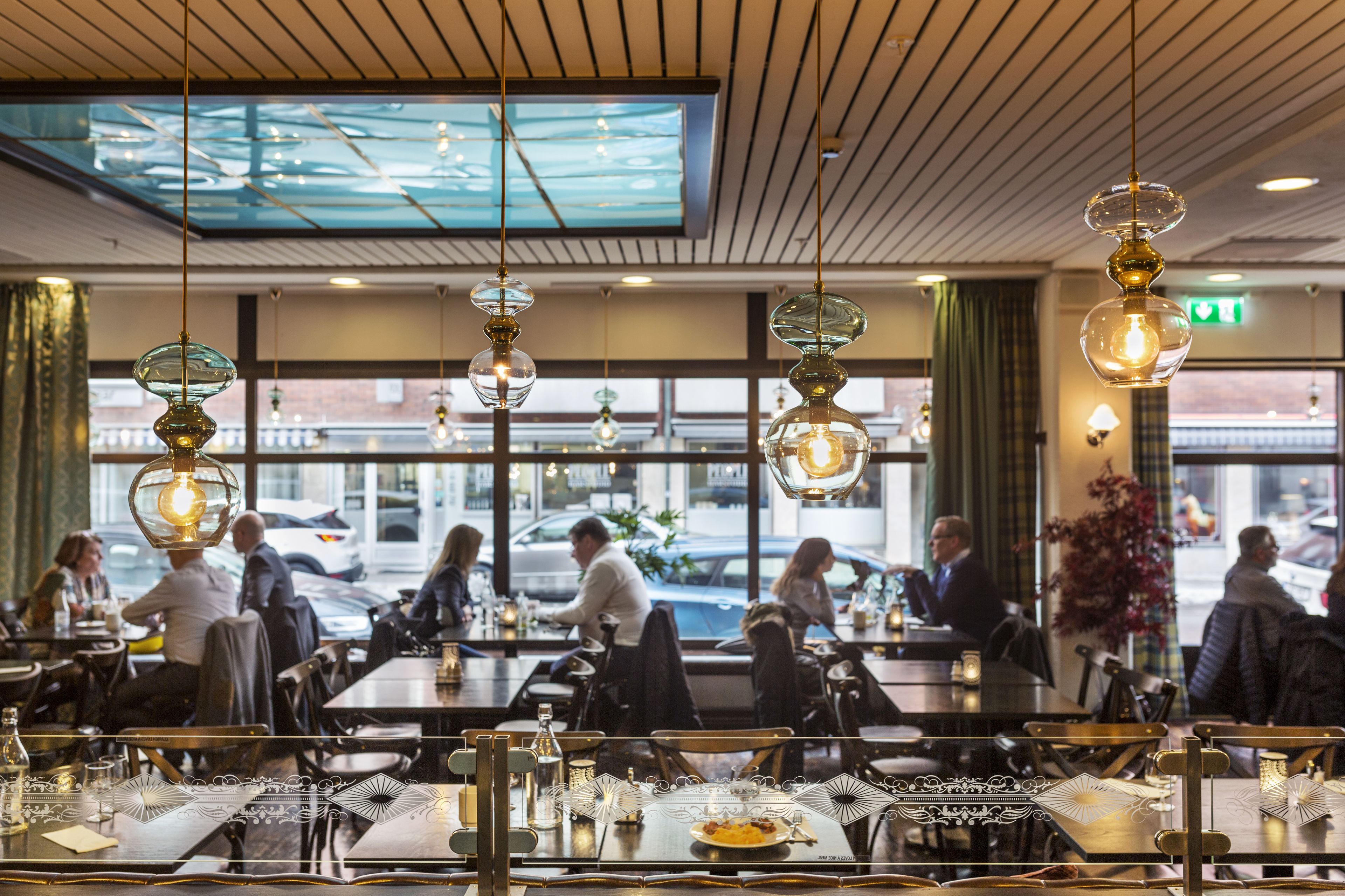 Een restaurant met glazen kroonluchters, grote ramen en uitzicht op de straat.