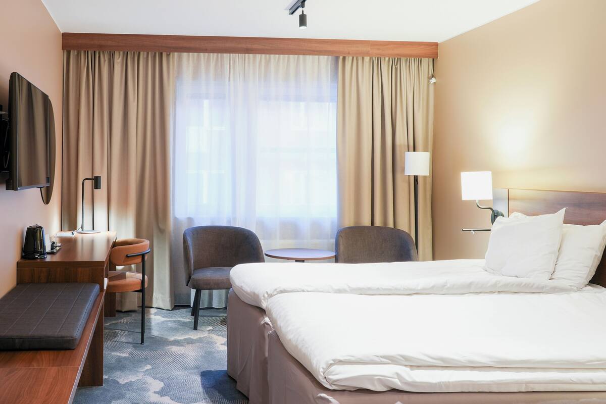 Hotellihuone, jossa on sänky, työpöytä, tuoli, pieni pöytä ja televisio.