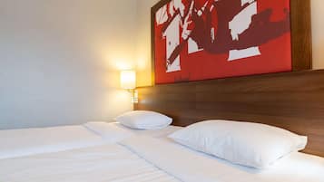 A hotel room with a neatly made bed, a wall-mounted light, and a large abstract painting above the bed.