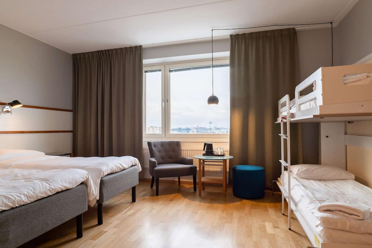 A hotel room with two beds, a chair, a small table, and a bunk bed.