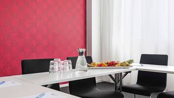 Uma sala de conferência com uma mesa branca, cadeiras pretas, um jarro de água e um prato de frutas.
