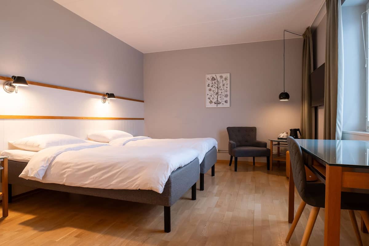A modern hotel room with a large bed, a desk, a chair, and a flat-screen TV.