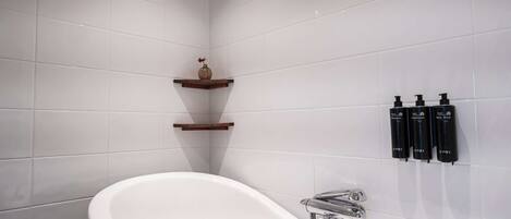 Un baño moderno con una bañera independiente, paredes de azulejos blancos y un estante de madera con un florero.