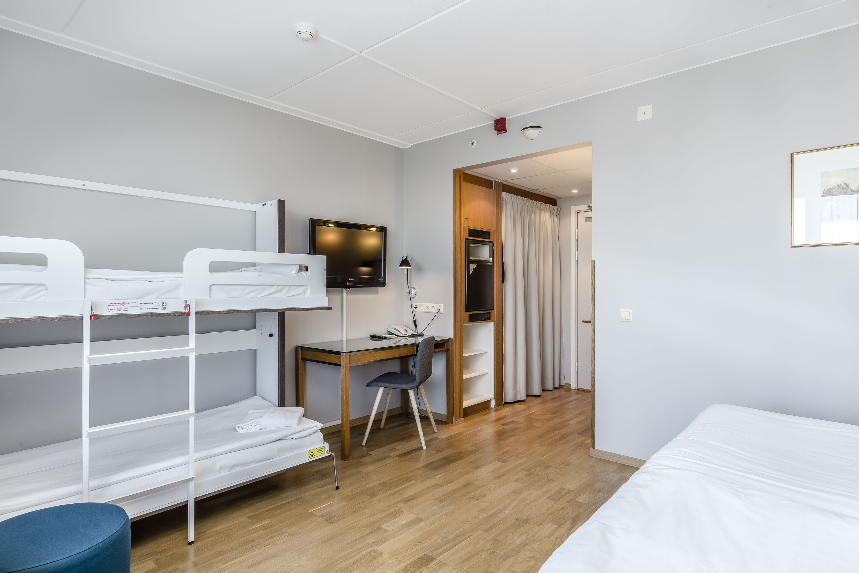 Habitación de hotel con literas, un escritorio con silla, televisión y una cama.