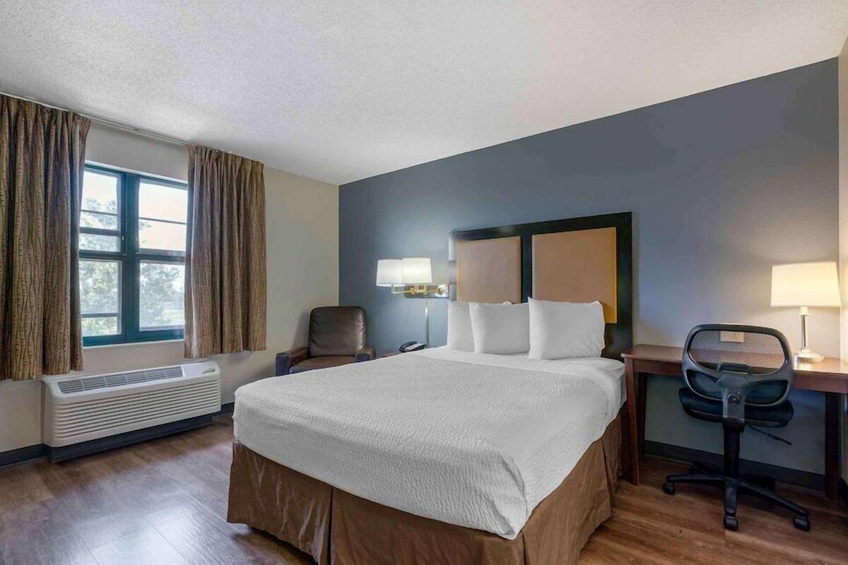 Een hotelkamer met een groot bed, een bureau, een stoel, een lamp en een raam met gordijnen.
