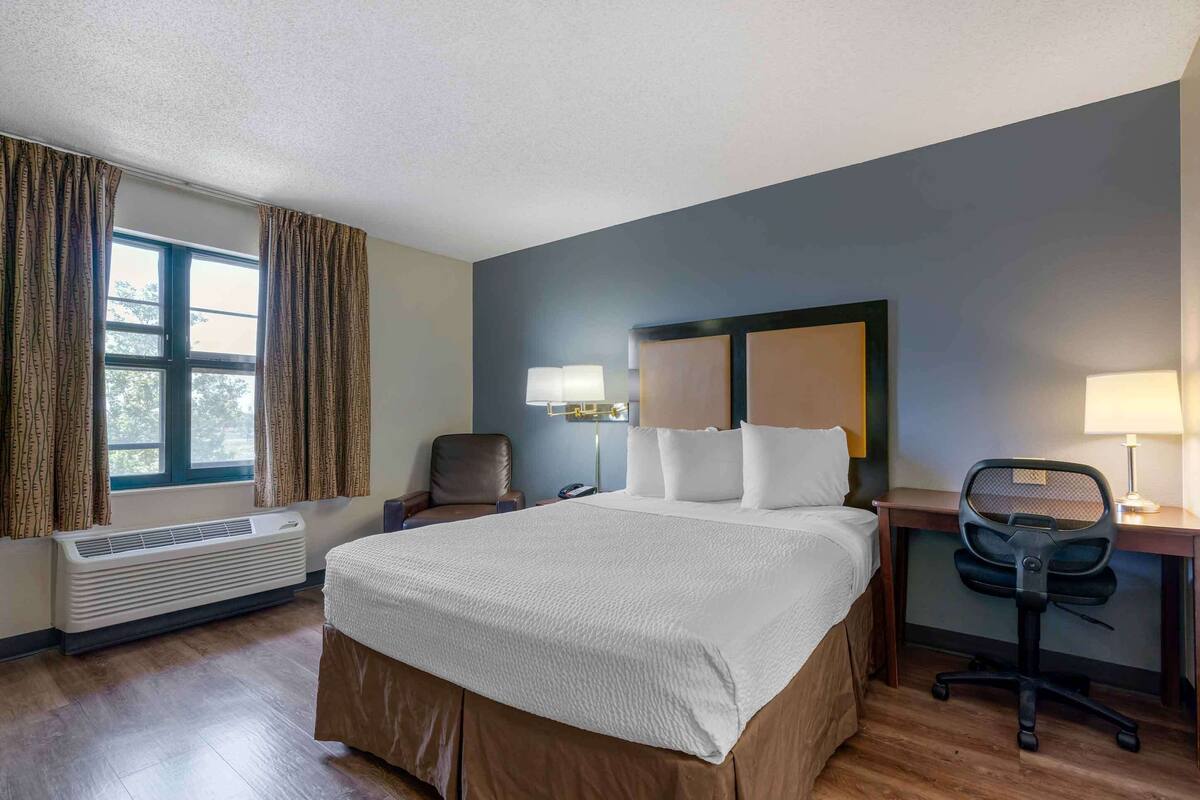 Een hotelkamer met een groot bed, een bureau met stoel, een bureaulamp en een raam met gordijnen.