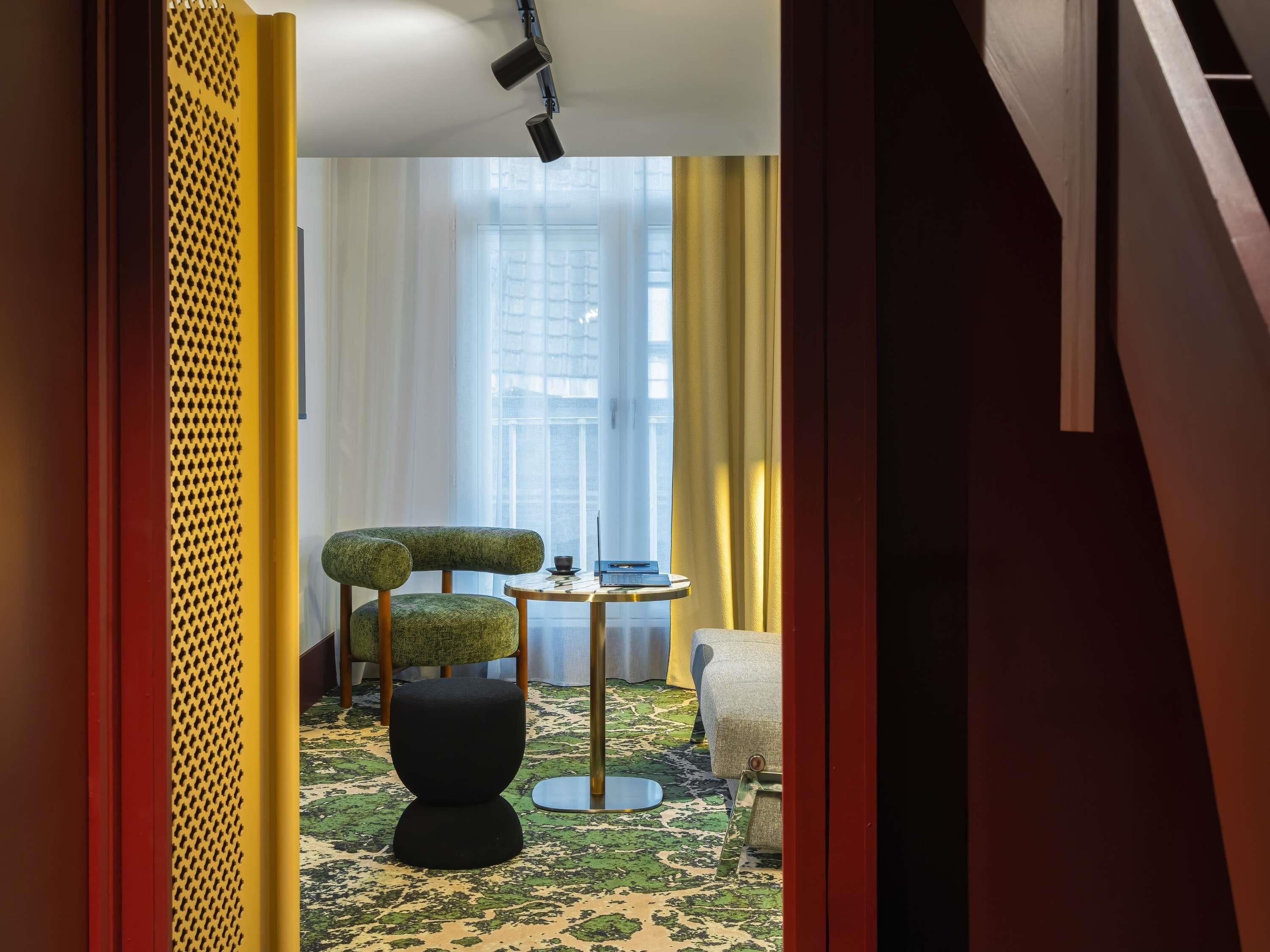 A modern hotel room with a unique green and black chair, a small round table, and a decorative floor lamp.