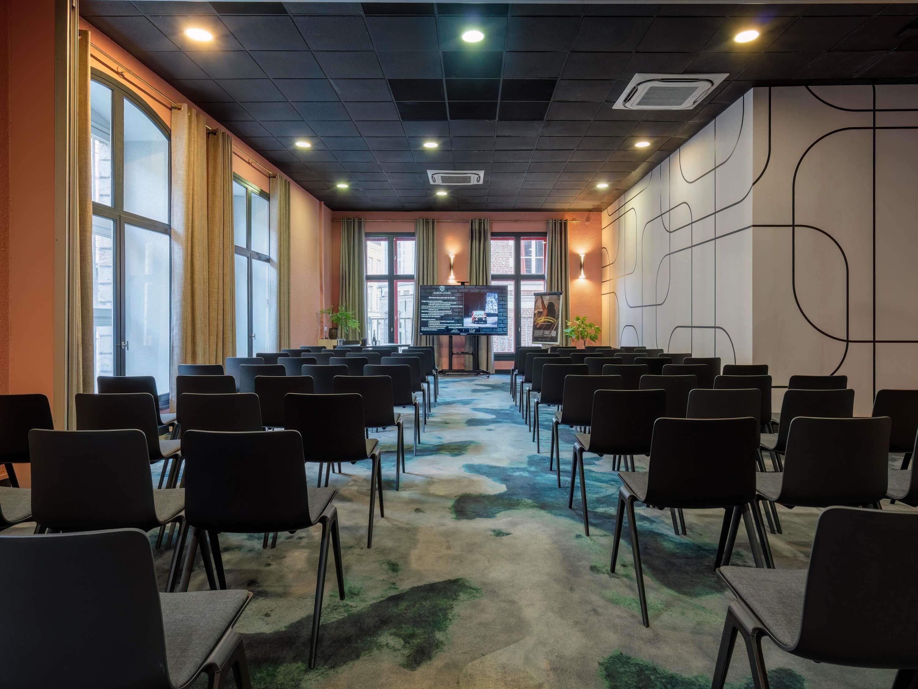 A conference room with rows of chairs, a large screen, and a window with curtains.