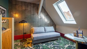Een moderne kamer met een grijze bank, een vloerlamp, een kamerkleed met dessin en uitzicht door een dakraam.
