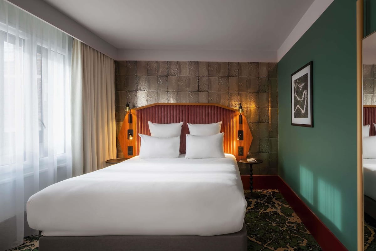 Une chambre d’hôtel avec un grand lit, une table de chevet, un miroir et un mur d’accent vert.