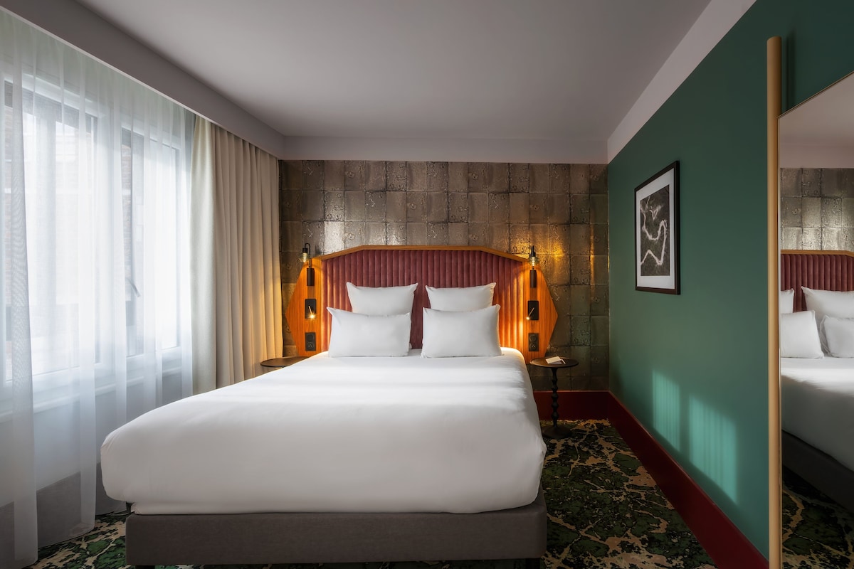 Habitación de hotel con una cama grande, cabecero con luces, pared de acento verde y un espejo amplio.